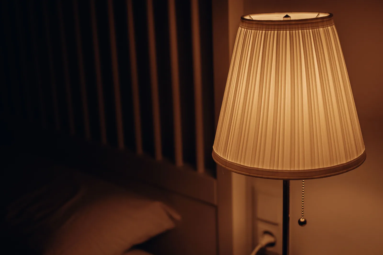 A warm bedside lamp lit in an otherwise dark bedroom, with the edge of a pillow just visible beside it.
